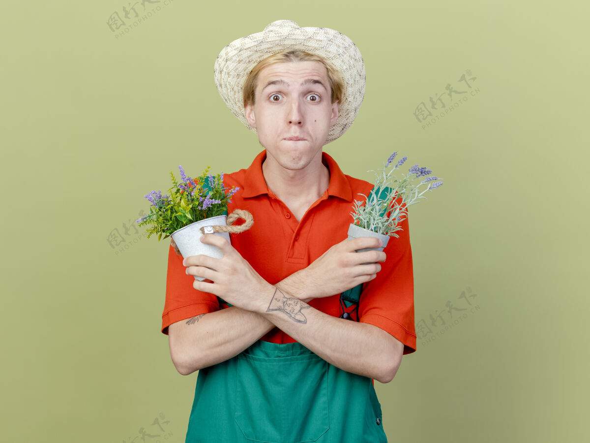 植物年轻的园丁 穿着连体衣 戴着帽子 手里拿着盆栽植物花园困惑灯光