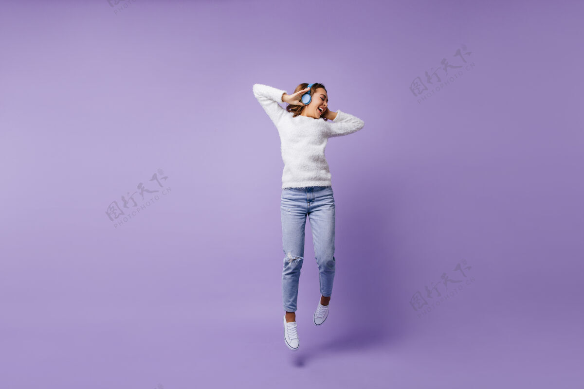 智能手机意气风发的幸运女学生跳伞穿着时尚白色毛衣和浅蓝色牛仔裤的女孩的全身画像全长休闲女性