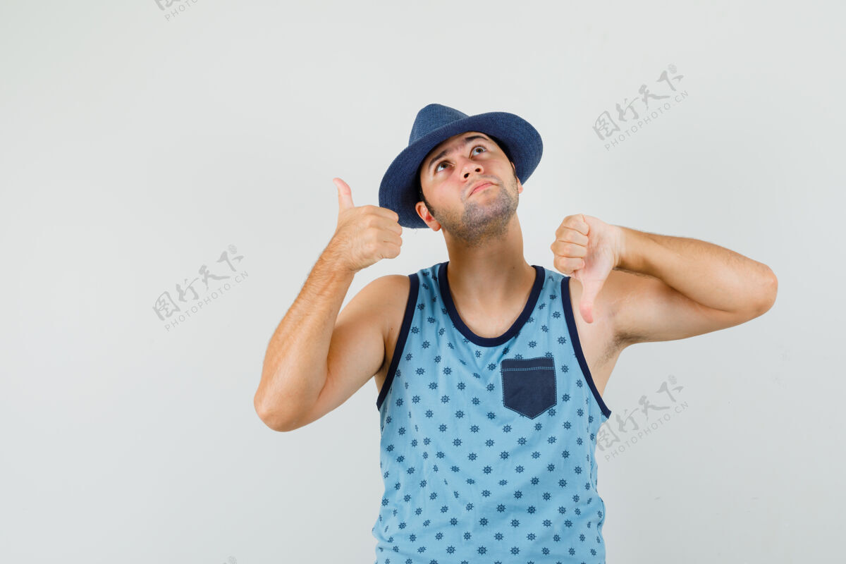 朋友年轻人穿着蓝色的单件上衣 戴着帽子 上下竖起大拇指 神情沉思正视图男人拇指时尚