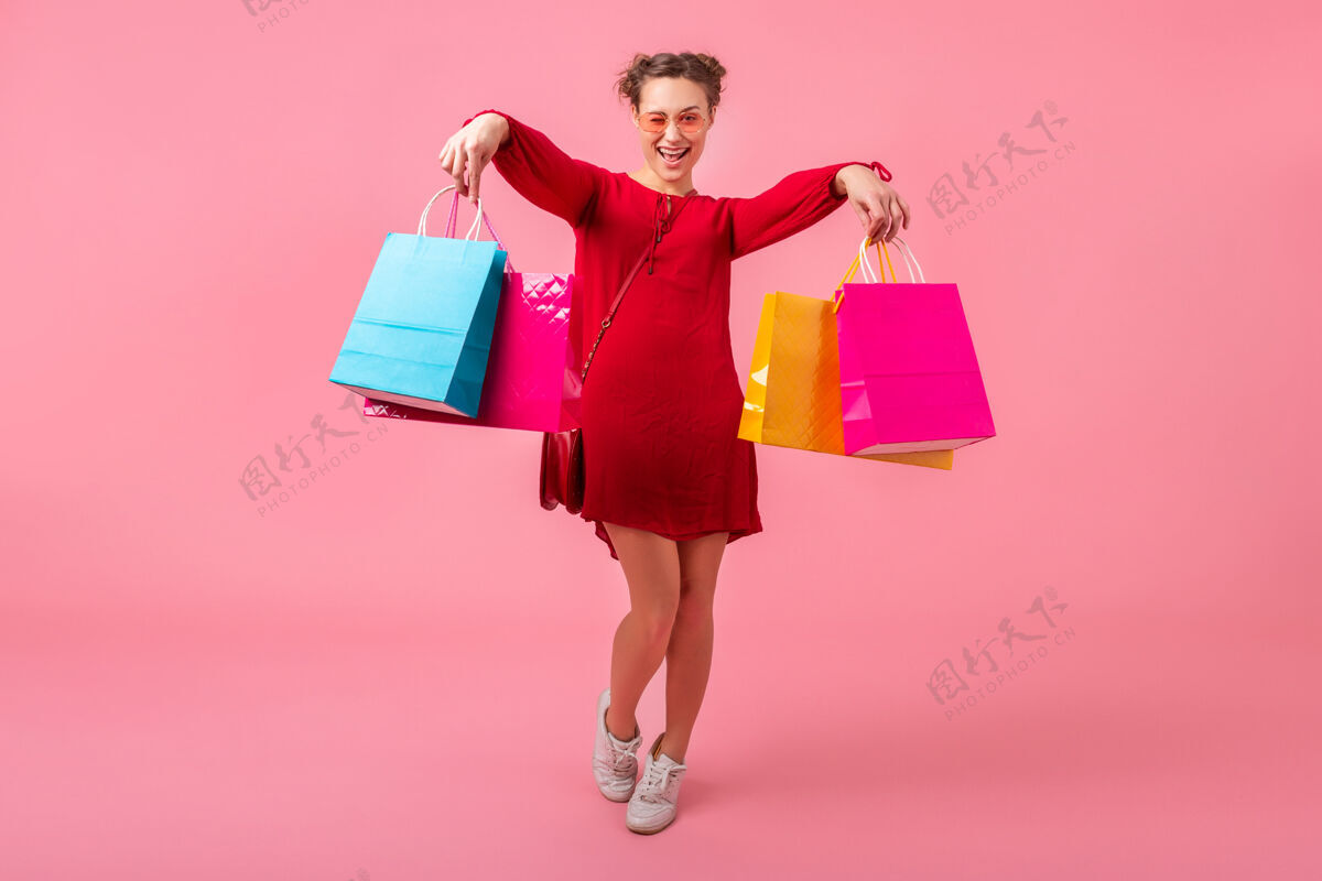 衣服迷人快乐微笑的时尚女性购物狂身着红色新潮连衣裙手持五颜六色的购物袋贴在粉色的墙上 销售兴奋 春夏时尚潮流夏天欢呼微笑