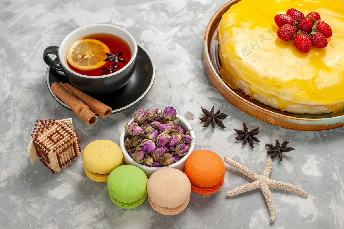 烘焙半俯瞰美味的水果蛋糕 黄色糖浆 法国马卡龙和一杯茶放在白色的桌子上杯子半顶生的
