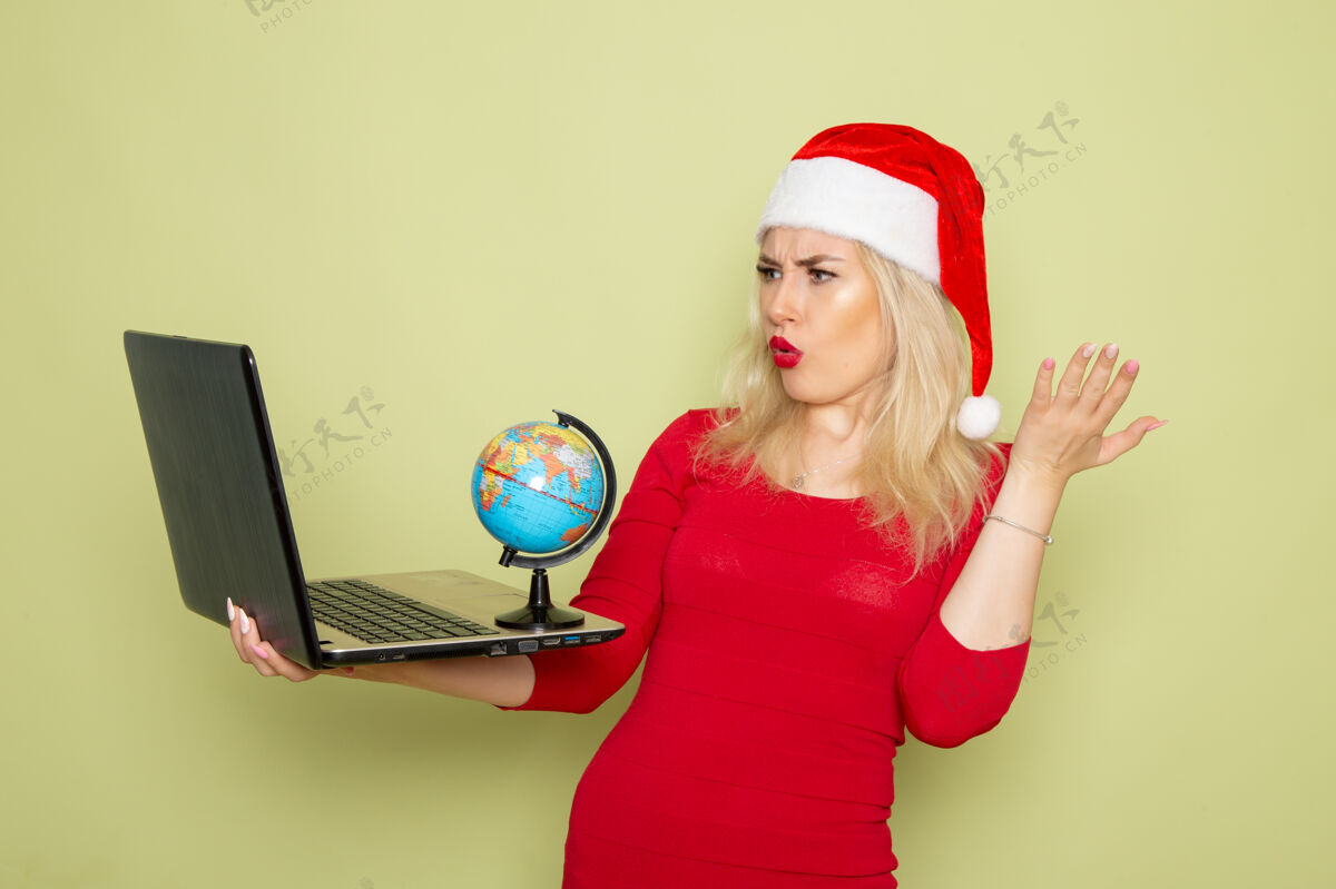 雪正面图漂亮的女人拿着地球仪 在绿色的墙上用笔记本电脑圣诞色雪地假日新年的情绪肖像视图情感
