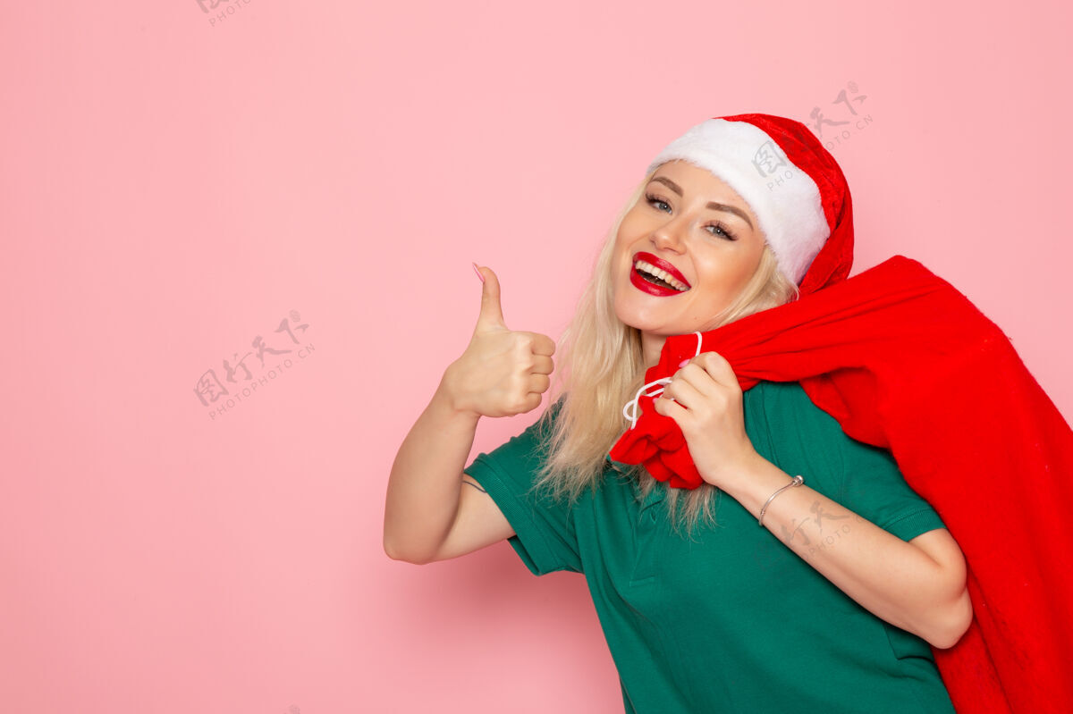 风景正面图年轻女性提着红包带着礼物在粉色墙上模型假日圣诞新年照片彩色圣诞老人肖像颜色美丽