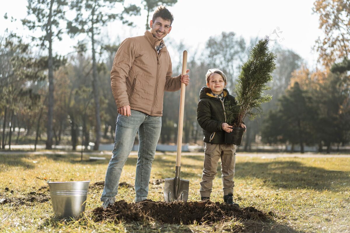 水平男人一边用铲子挖洞种树 一边在儿子旁边摆姿势父亲农业男孩