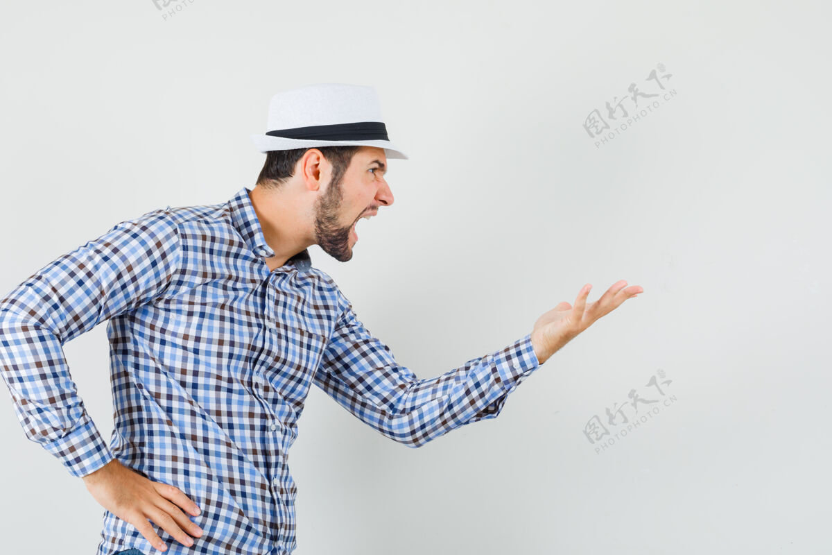 站立一个穿着格子衬衫 戴着帽子的年轻人冲着某人大喊大叫 看上去很愤怒 正对着他看成功欢呼帽子