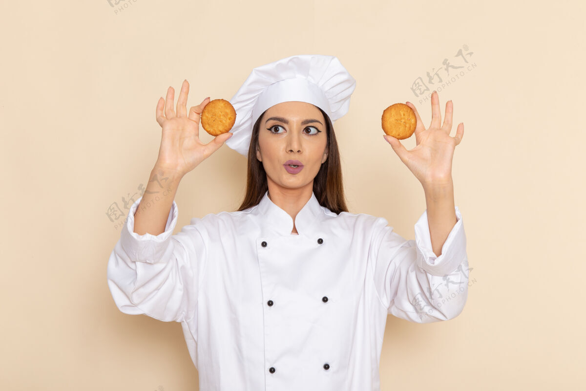 成人身穿白色厨师服的年轻女厨师正拿着饼干站在白墙上专业微笑肖像