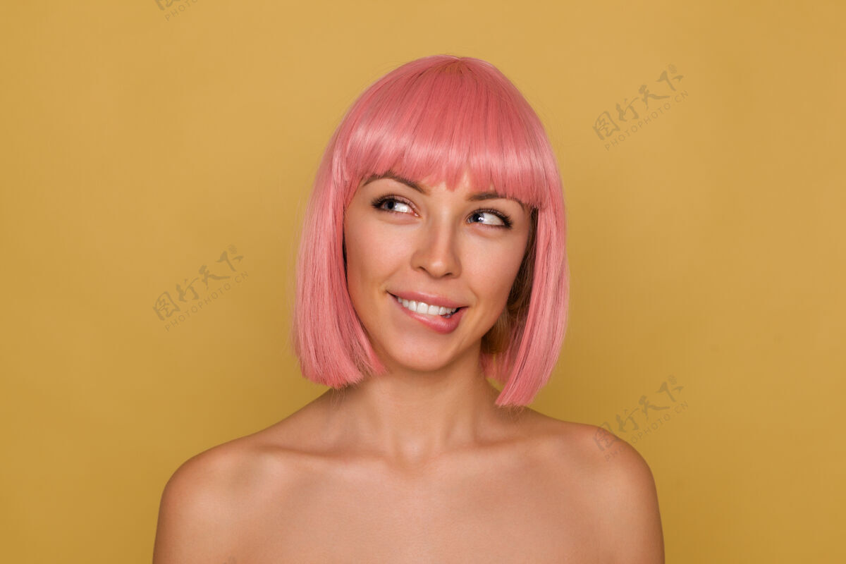 欢呼年轻迷人的正面女士的肖像 粉色时髦的鲍勃发型 一边梦幻般地看着一边咬着内衣 一边眯着蓝眼睛 一边在芥末色背景上摆姿势鲍勃粉色前锁