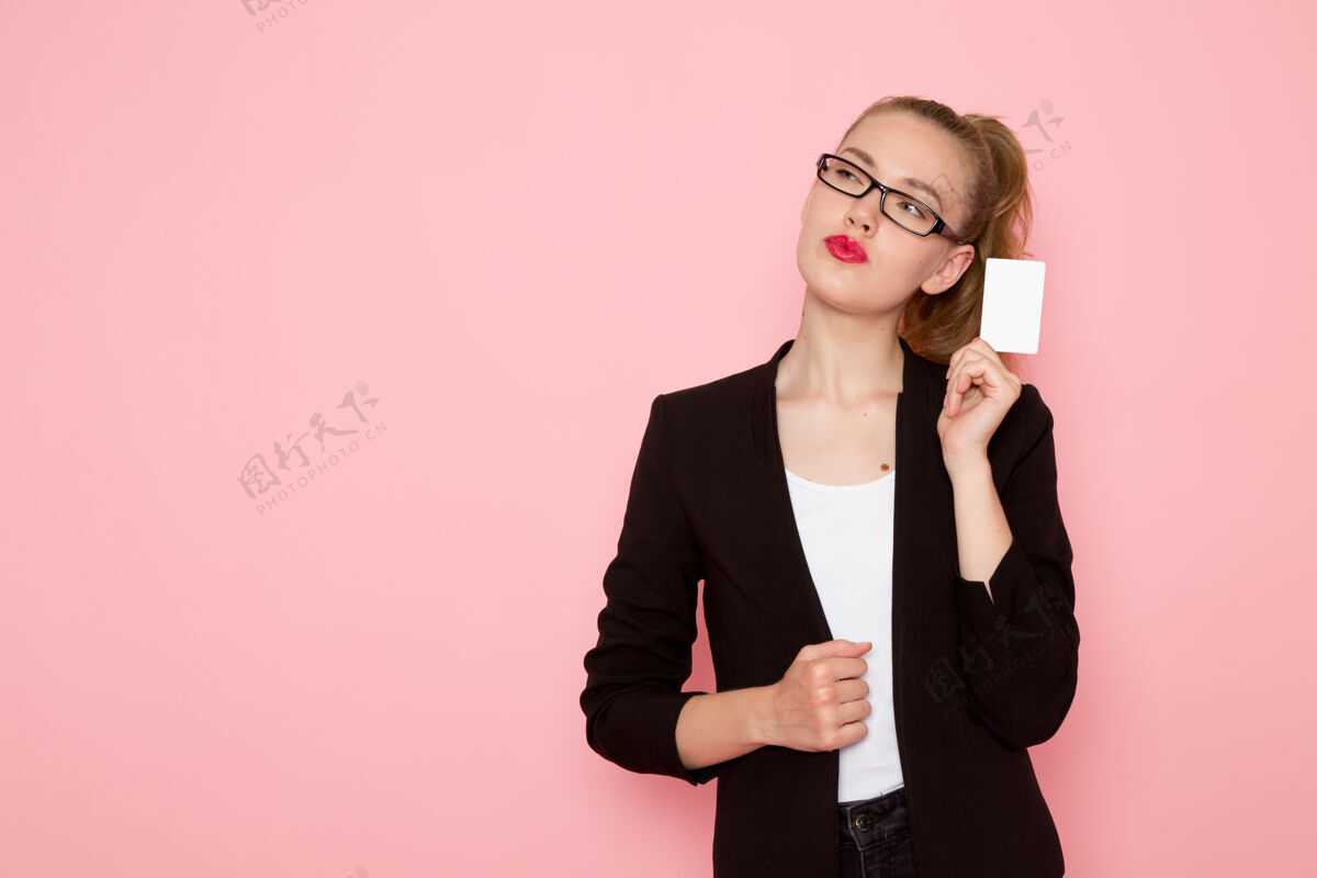模型身穿黑色夹克的女上班族正拿着粉色墙上的白卡思考严格办公室女
