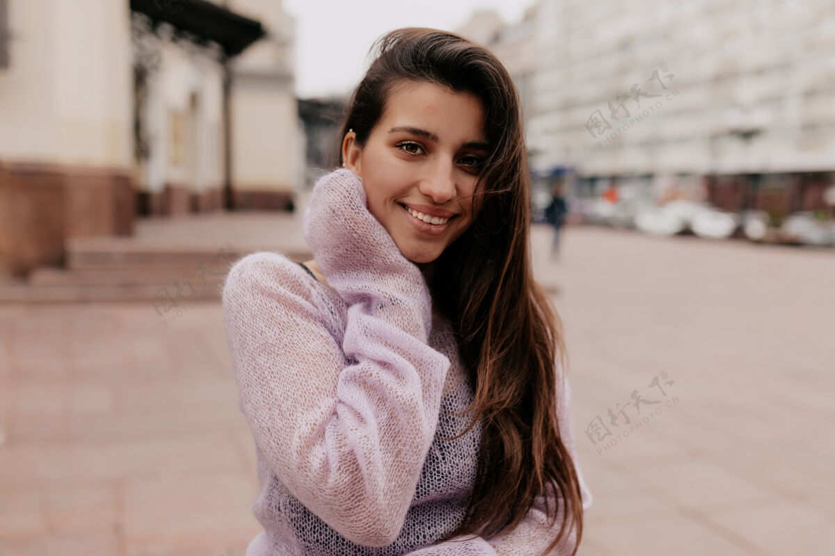 学生微笑的快乐女人 留着长发 穿着紫罗兰色毛衣 在古老的建筑物上摆姿势美丽表情自信