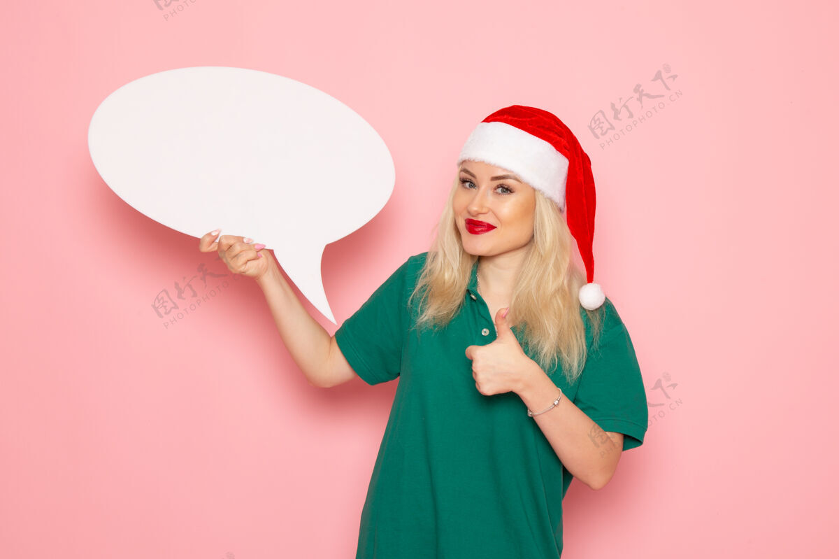 年轻的女人正面图年轻女子手持白色大招牌在粉色墙上女士赠送雪彩照片新年假期漂亮圣诞节风景