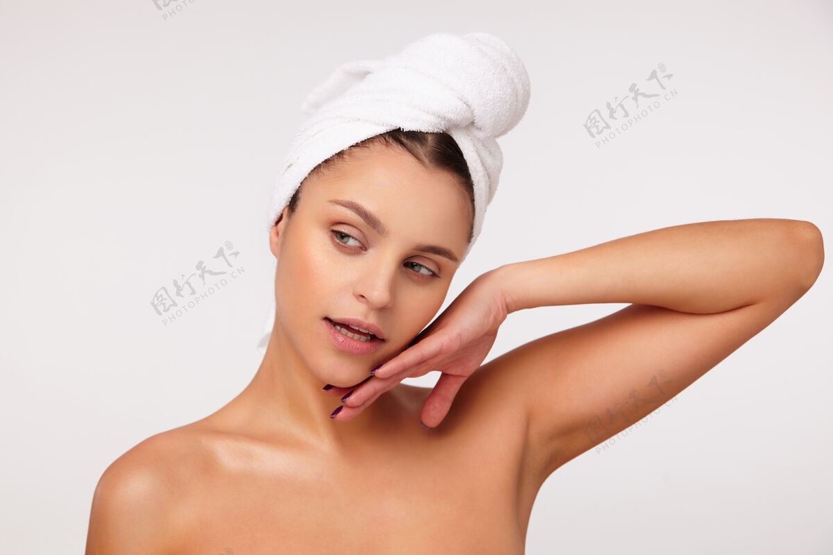 情绪一幅美丽的年轻黑发女子的画像 她头上戴着浴巾 一边看着一边 轻轻地抚摸着她的脸 赤裸着肩膀站在白色的背景上肖像手站立