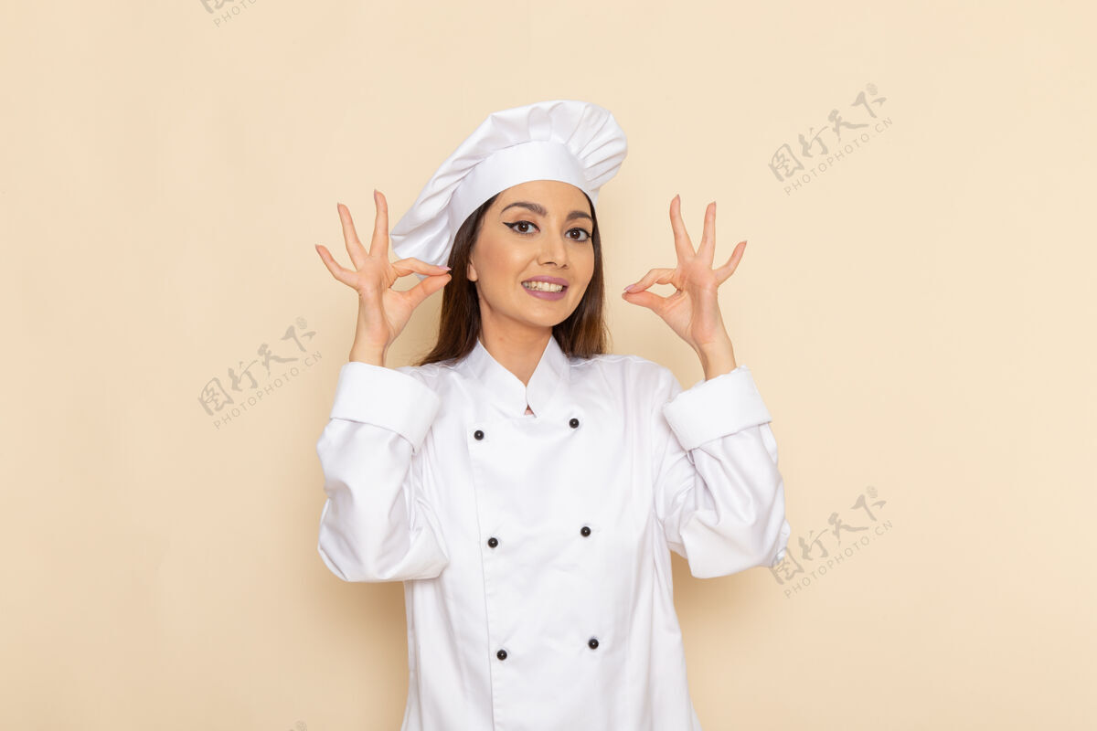 膳食身着白色厨师服的年轻女厨师在浅白的墙上微笑的正面视图微笑工作年轻