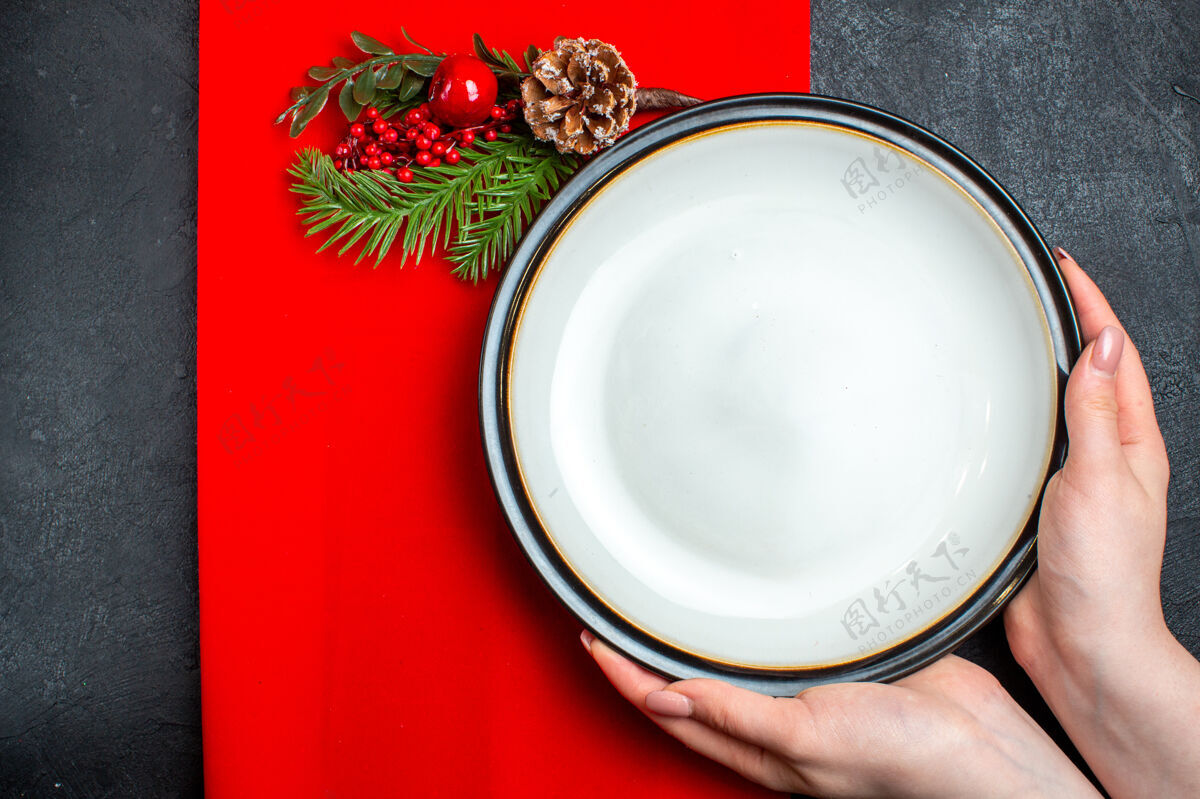 碗手拿空盘子和杉木枝装饰配件针叶树锥上的红色餐巾在黑暗的背景俯视图瓷器圣诞节瓷器