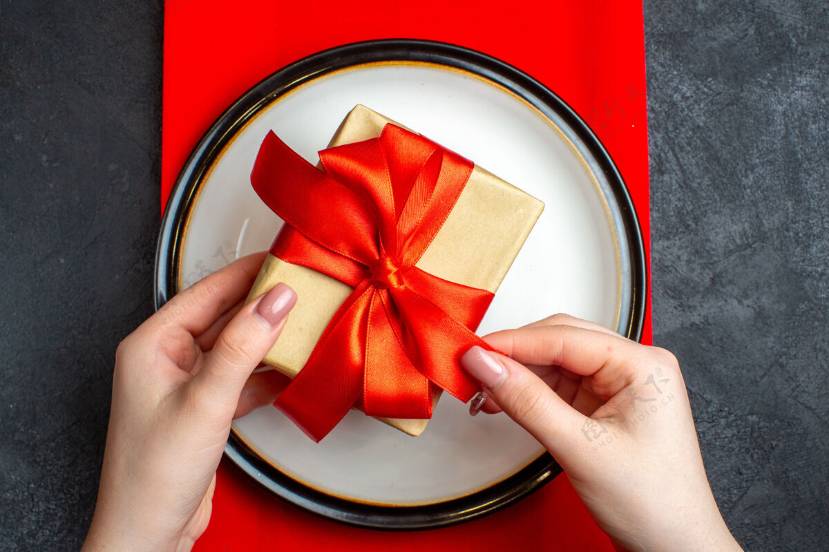 空盘子国家圣诞餐背景俯视图 黑色桌子上的红色餐巾上 手拿着空盘子 蝴蝶结形状的红丝带弓形顶部弓