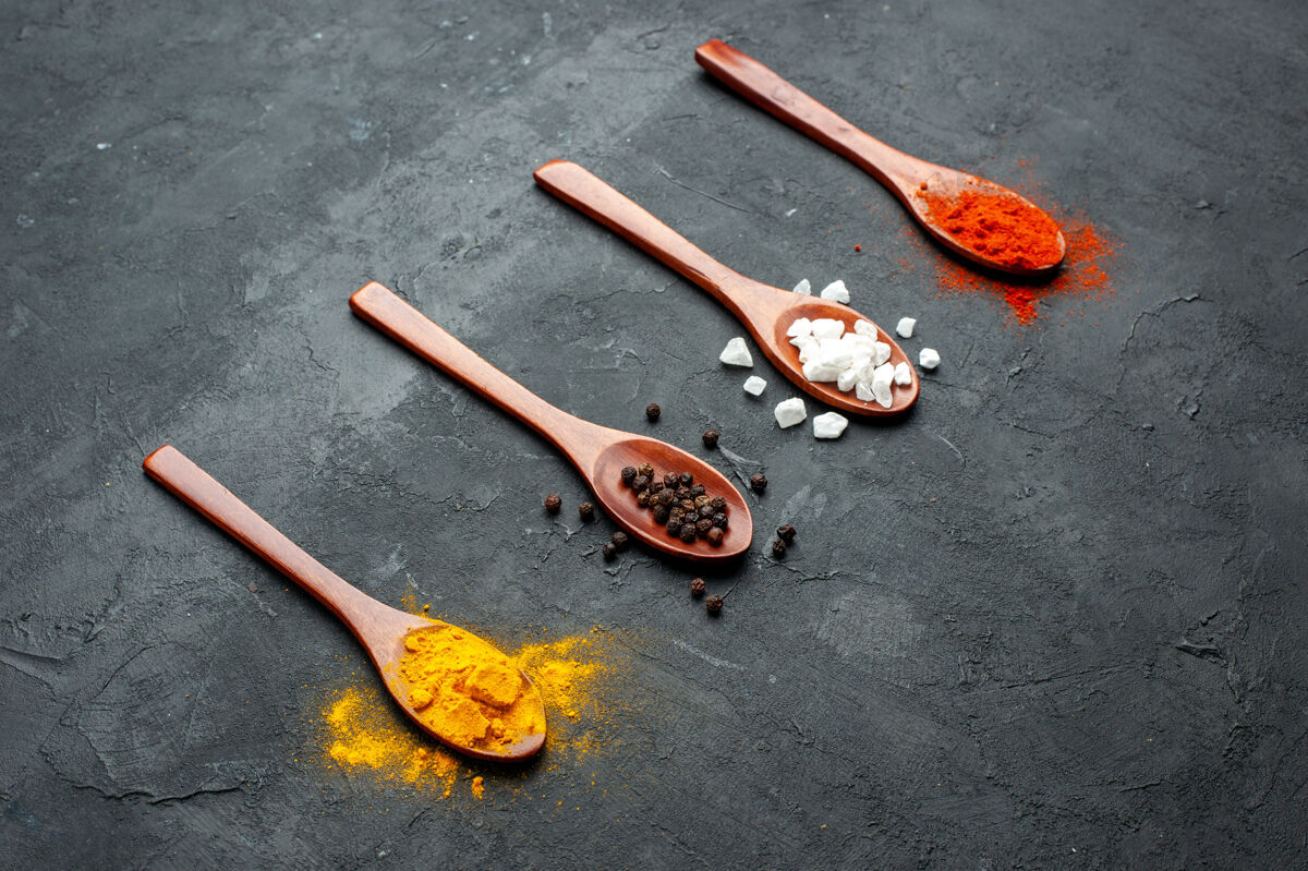 胡椒底视图斜排木勺 黑表面涂有姜黄黑胡椒粉和盐红胡椒粉勺子木勺观点
