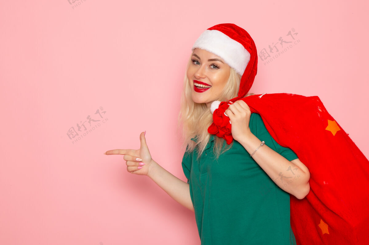 携带正面图：年轻女性手拿红包 粉色墙壁上有礼物节日模型圣诞节新年彩色圣诞老人肖像颜色风景
