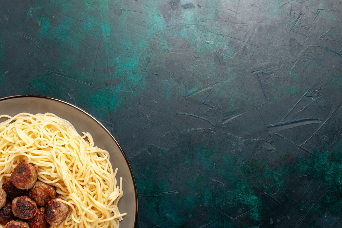 意大利面在深蓝色的桌子上俯瞰煮熟的意大利面食和肉丸生的意大利面意大利面