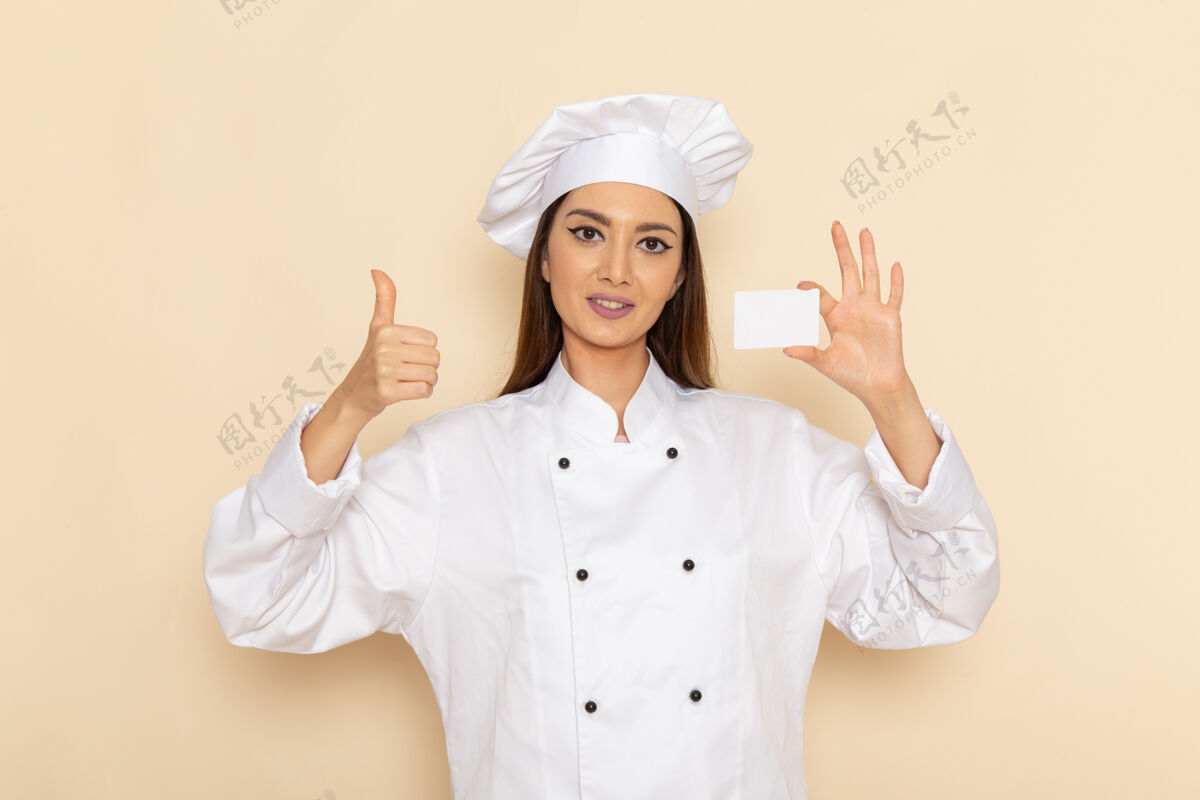 烹饪身穿白色厨师服的年轻女厨师手持白色卡片站在浅白的墙上西装年轻人工作