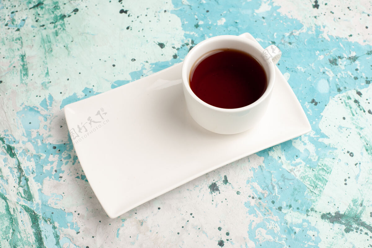 桌子浅蓝色桌子上的茶杯和盘子里有半杯茶热的饮料咖啡因