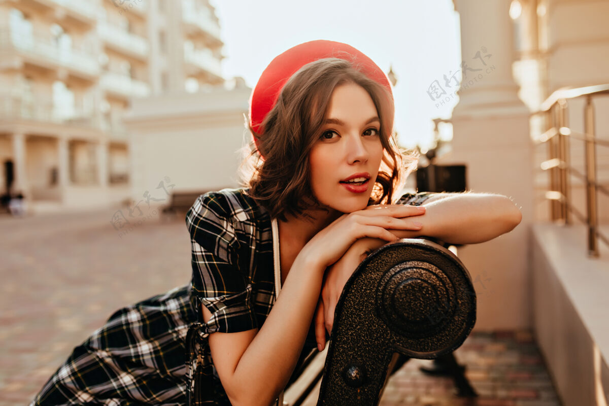情绪梦幻的法国女孩在长椅上摆姿势坐在城市里的温文尔雅的卷发女模特的户外肖像年轻微笑黑发