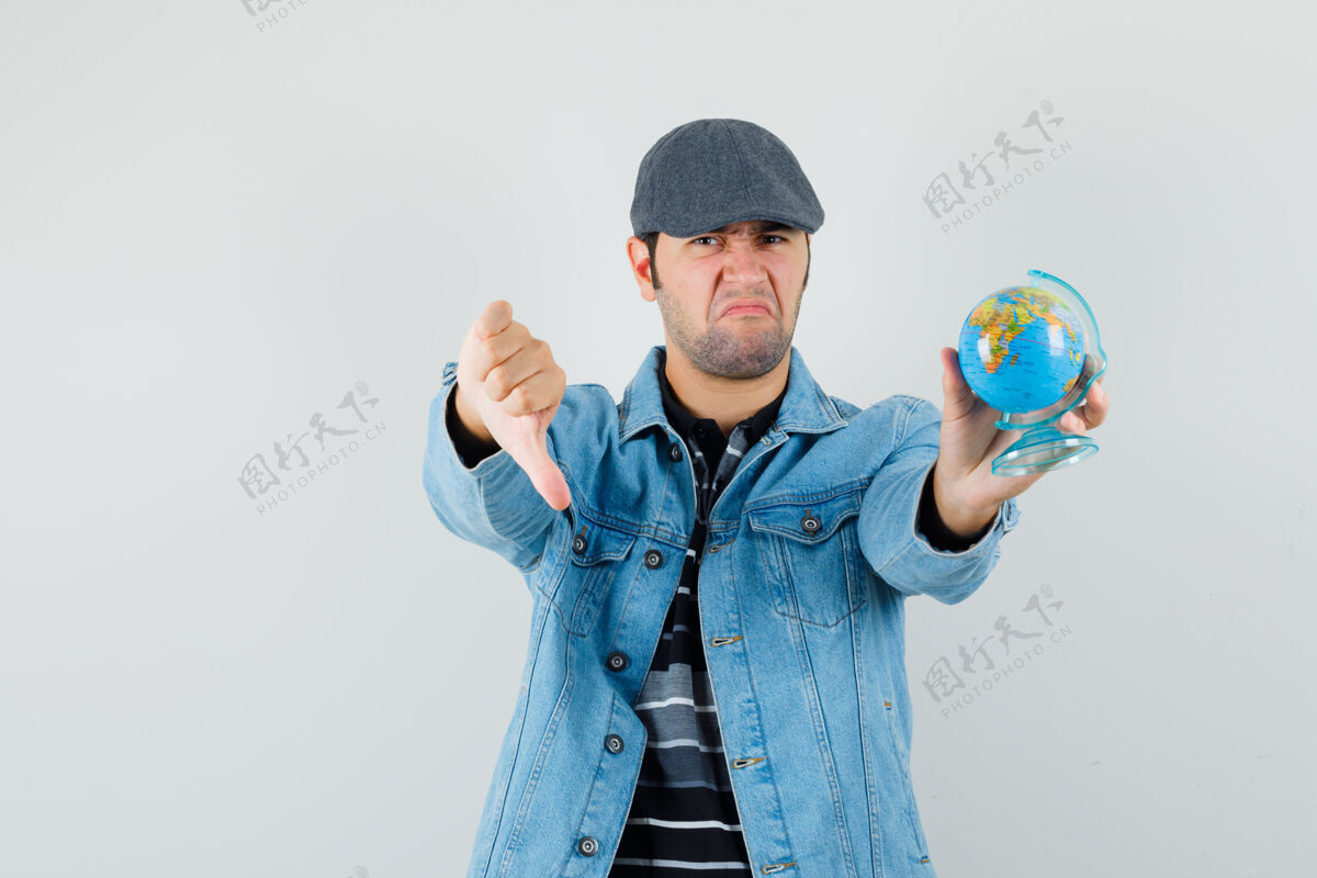 胡茬年轻人穿着夹克 戴着帽子拿着地球仪 拇指朝下 看上去很不高兴胡须男信心