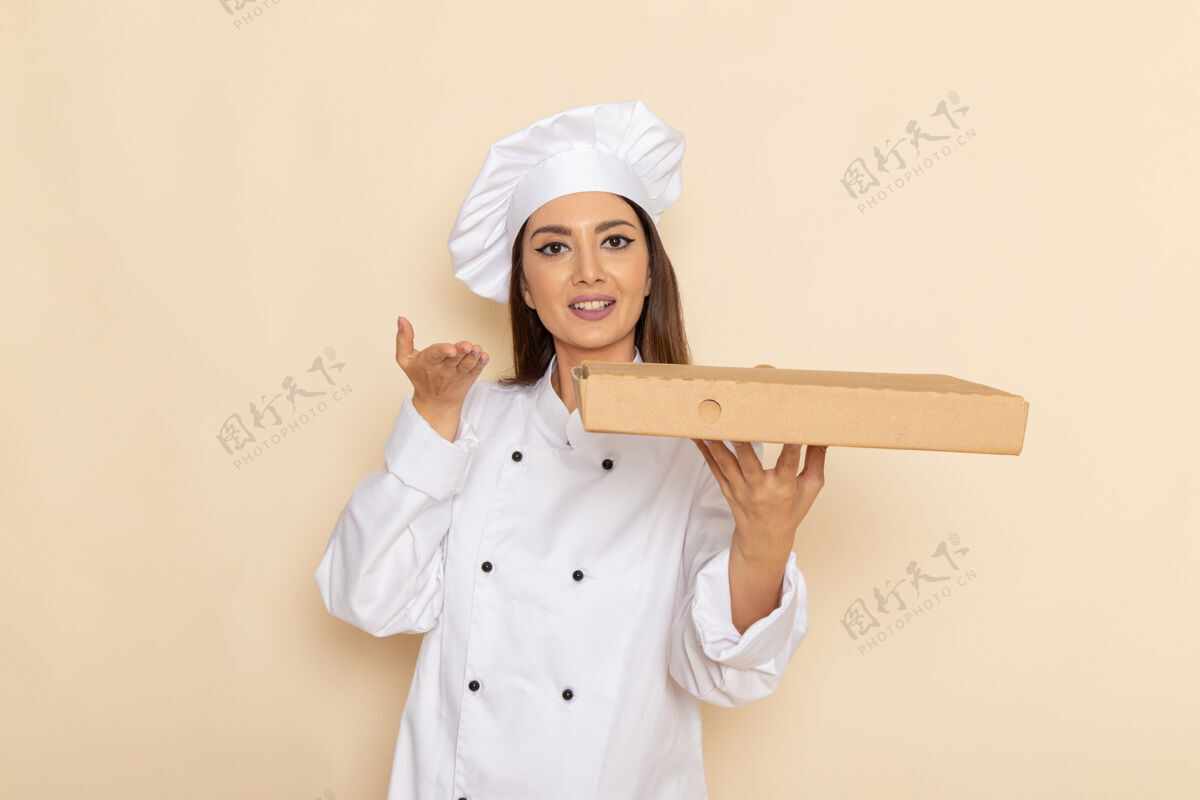 人身穿白色厨师服的年轻女厨师正拿着食物递送箱站在浅白的墙上女性工作烹饪