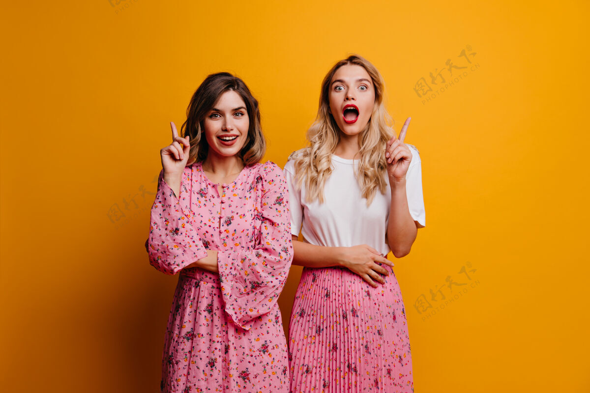 肖像对时髦服装感兴趣的女士在明亮的墙壁上摆姿势好奇的女性朋友站在黄色墙壁前的画像朋友时尚黑发