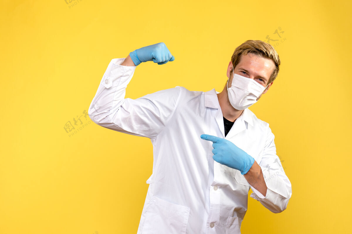 大流行正面图：男性医生在黄色背景病毒大流行的covid健康面具上弯曲视图成人弯曲