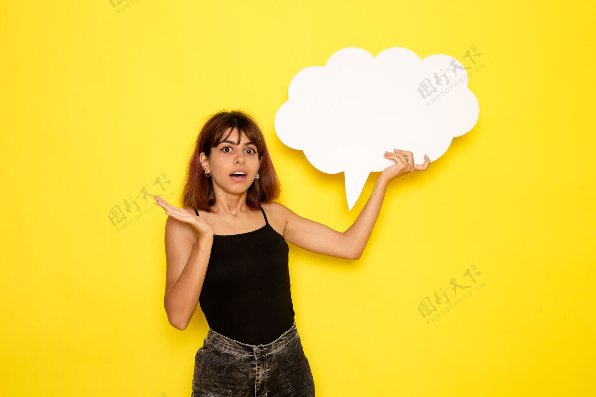 前面身穿黑色衬衫的年轻女性的正视图 在浅黄色的墙上举着大白字情绪姿势女孩