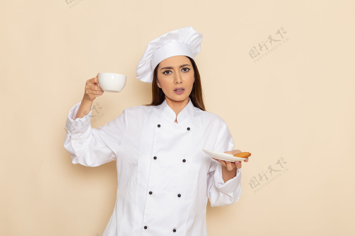 套装身穿白色厨师服的年轻女厨师正拿着一杯咖啡站在浅白的墙上女工作厨房