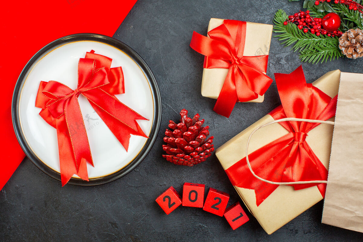 视图上图美丽的礼物和蝴蝶结形状的缎带放在一个板针叶树圆锥杉木树枝上 数字放在一张深色的桌子上圣诞圆锥体号码