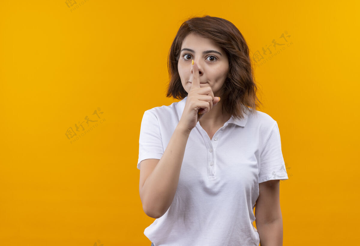 穿着一个短发女孩穿着白色马球衫 手指放在嘴唇上做着沉默的手势马球手指短发
