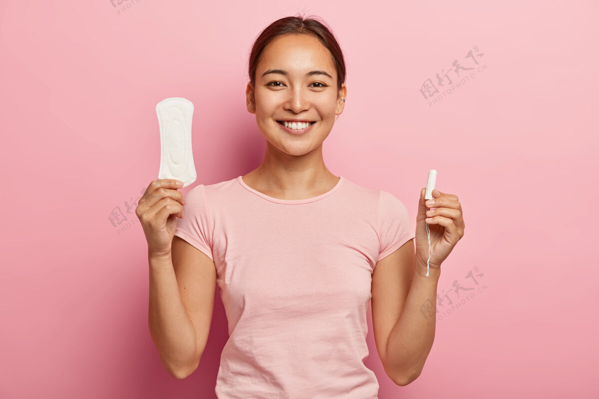 卫生棉条快乐韩国女人手握卫生巾和卫生棉条的水平镜头 展示女性健康的贴心产品 微笑温柔 穿着休闲装 有关键的日子玫瑰色休闲室内