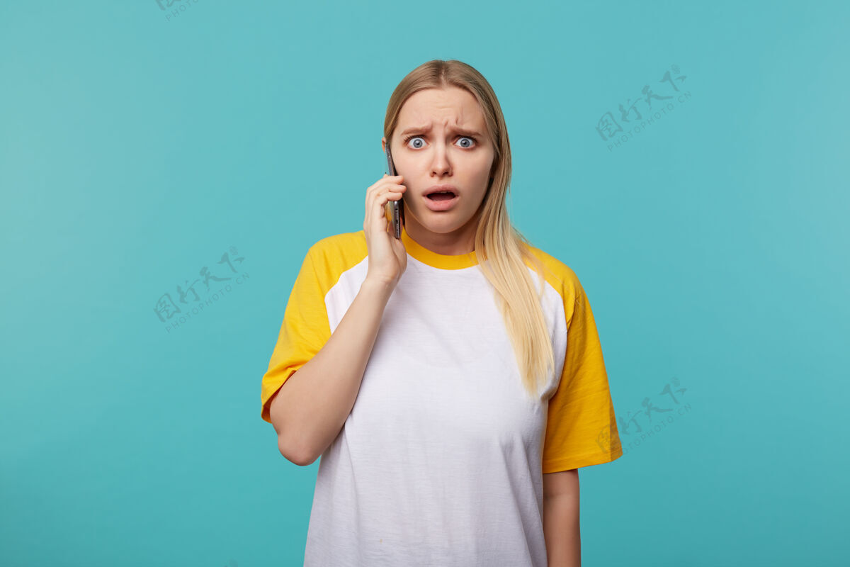 困惑困惑的年轻蓝眼睛白头发的女人随意的发型皱眉困惑的眉毛 同时听到令人震惊的消息在电话交谈 孤立的蓝色室内穿着女士