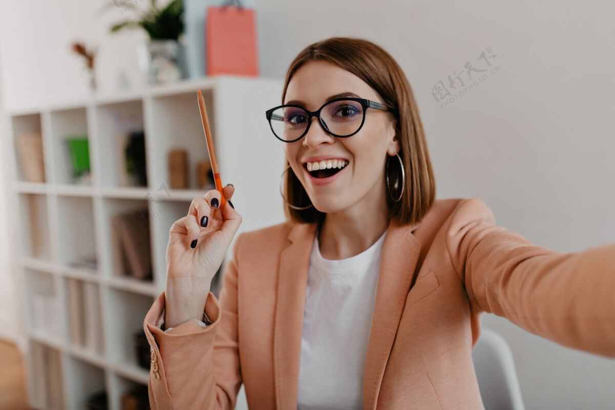 女性一位戴着眼镜 穿着时尚轻便服装的女商人 手里拿着橙色铅笔 自拍人员专业人士工作