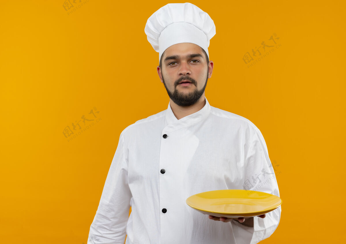 制服身着厨师制服的年轻男厨师手拿着空盘子 看上去孤立在橙色的空间里橙色厨师年轻