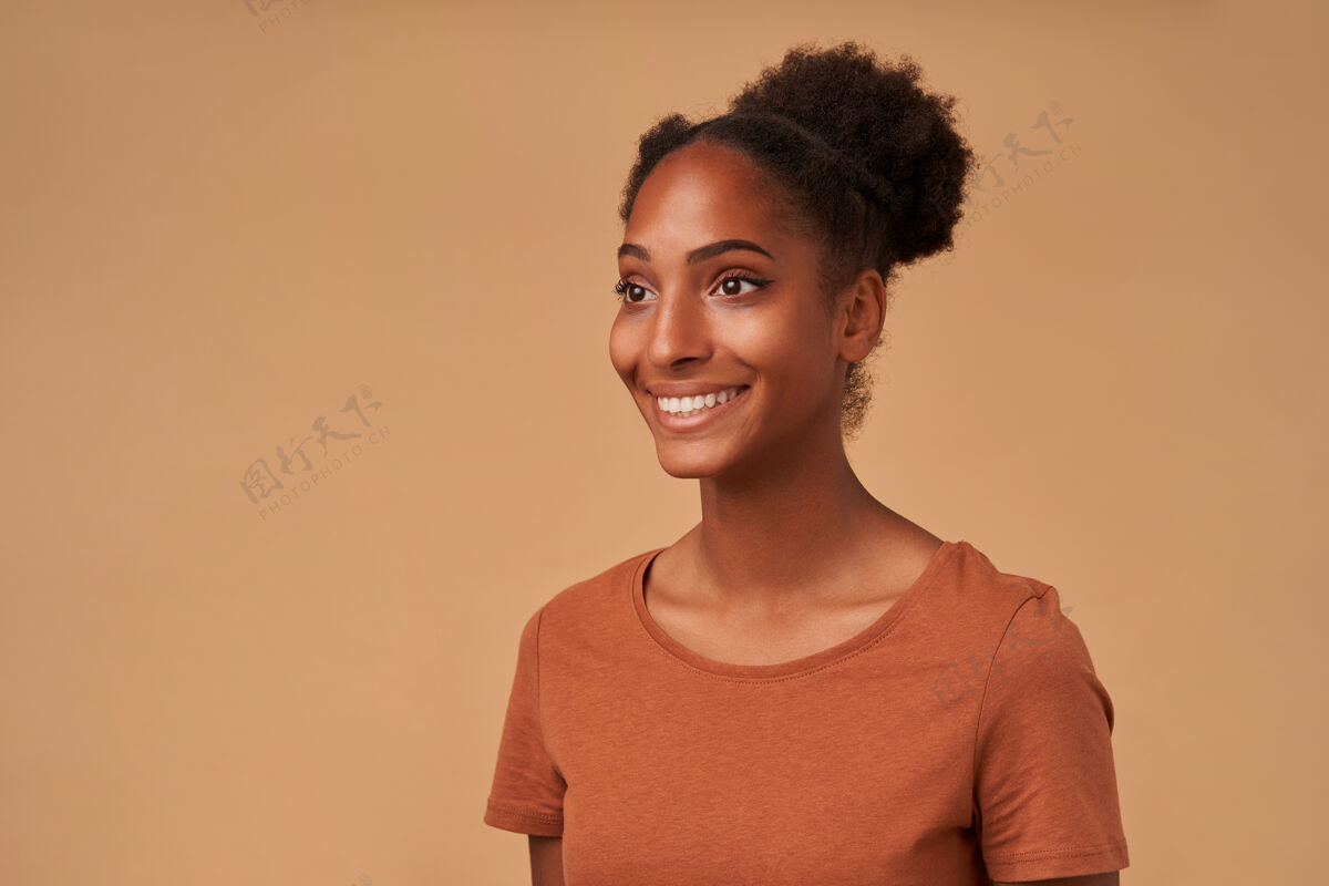女性年轻的黑皮肤卷发女子站在米色的青铜t恤上 带着迷人的微笑积极地看着一边的肖像卷发女士年轻