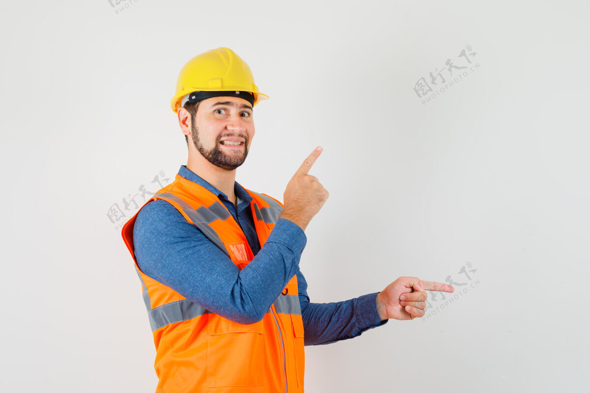 安全年轻的建筑工人穿着衬衫 背心 头盔 手指向上和侧面 看起来很高兴前视图男人工业工人