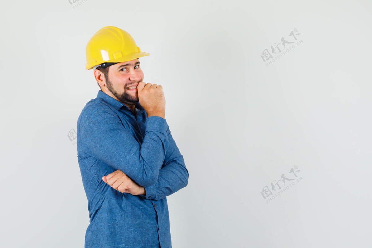羞愧年轻的工人穿着衬衫 戴着头盔站在思考的姿势 看上去很惭愧姿势讨论谈话