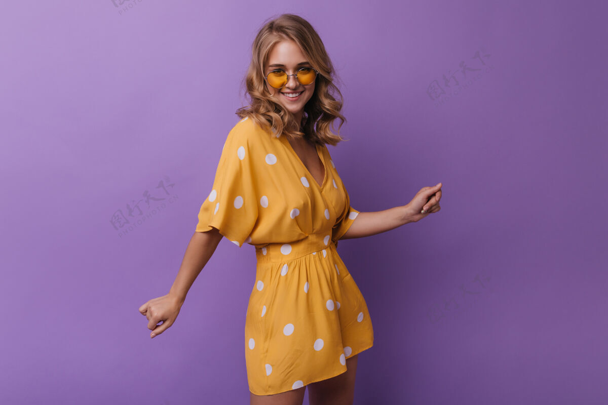 爱穿着复古橘色服装的可爱女人对着镜头笑着一幅壮观的女孩的肖像 一个波浪形的金发女孩被隔离在紫色上休闲时尚服饰
