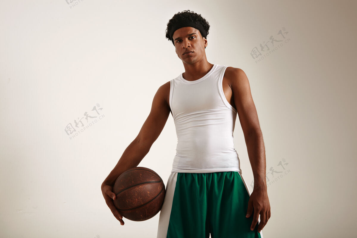 阳刚底图上的健美肌肉愤怒的非洲裔美国篮球运动员在白色和绿色制服举行一个垃圾篮球健身得分比赛