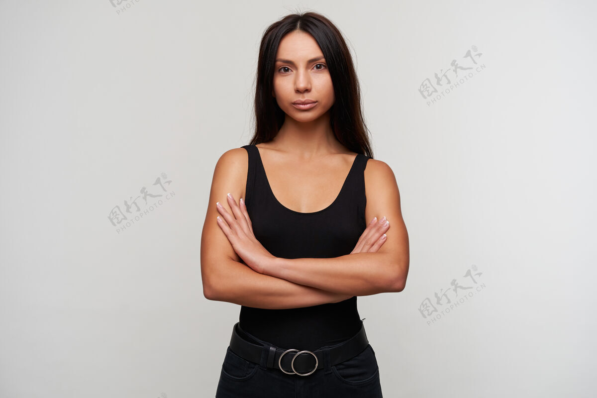 平静画中年轻漂亮的黑发女子 随意化妆 双手叠放在胸前 一边冷静地看着 身着黑色衣服 一边站在白色的地面上腰带裤子室内