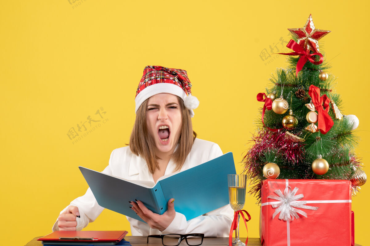 前面前视图女医生坐在圣诞礼物举行的黄色背景上的文件礼物快乐文件