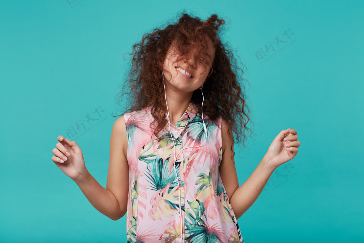 情绪可爱的年轻快乐的棕色卷发女士愉快地挥舞着她的头发 举手跳舞 在蓝色的夏季衬衫孤立高兴长女士