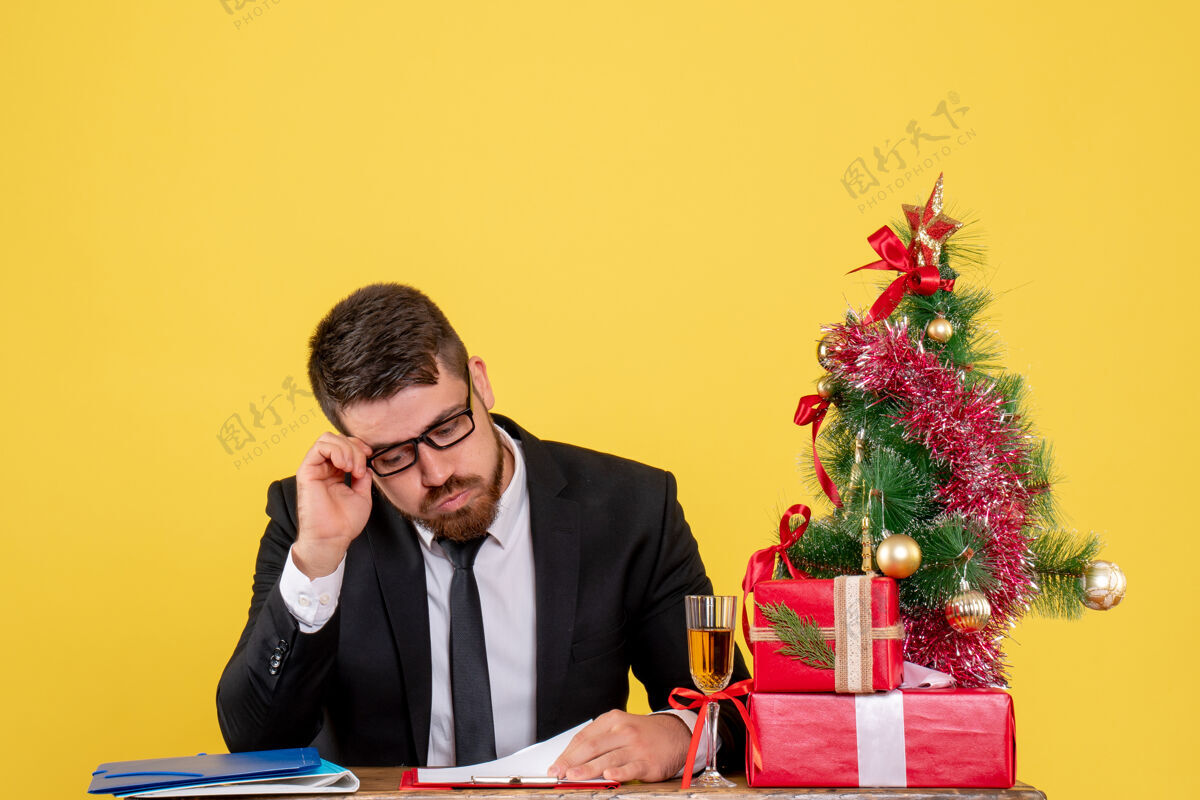 行政人员正面图：桌子后面的男工人拿着礼物 黄色的圣诞树礼物颜色新郎