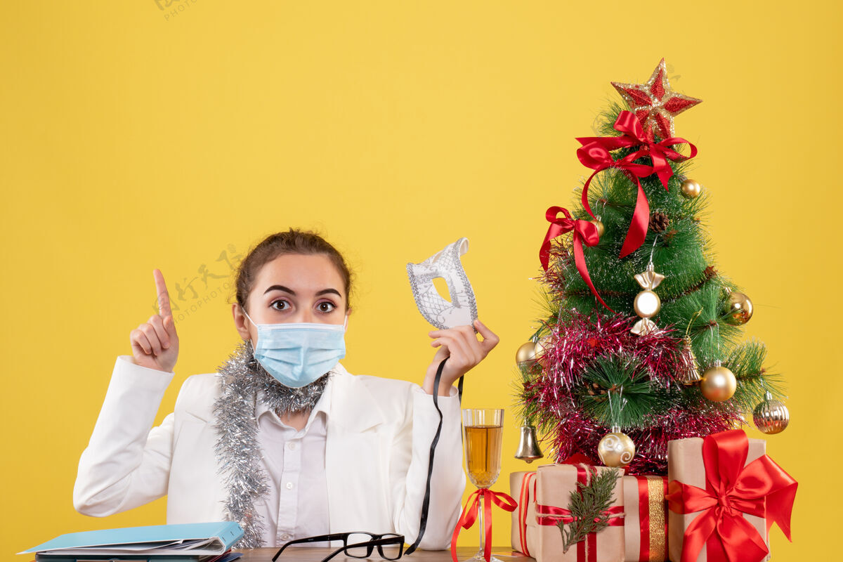脸正面图女医生戴着黄色背景的无菌口罩坐在圣诞树和礼盒里健康前面背景