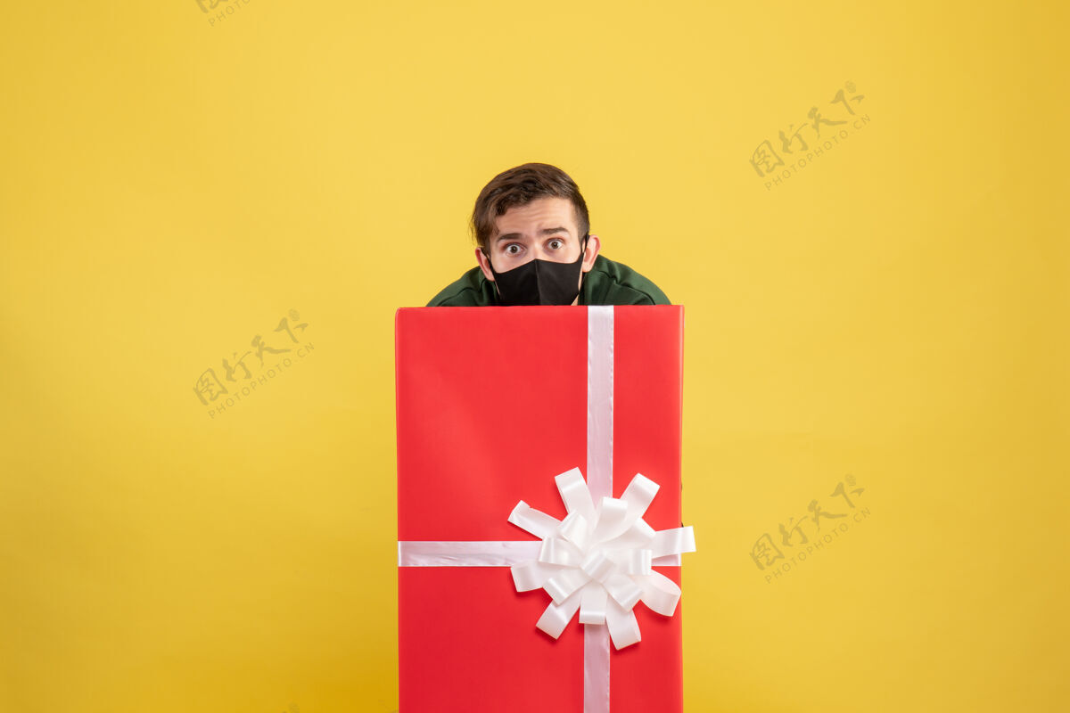 丝带正面图：年轻人躲在黄色的大礼品盒后面大购物者年轻人