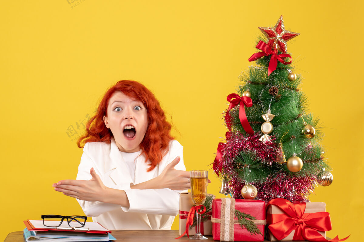插花前视图：女医生坐在桌子后面 黄色背景上有圣诞礼物桌子坐着人