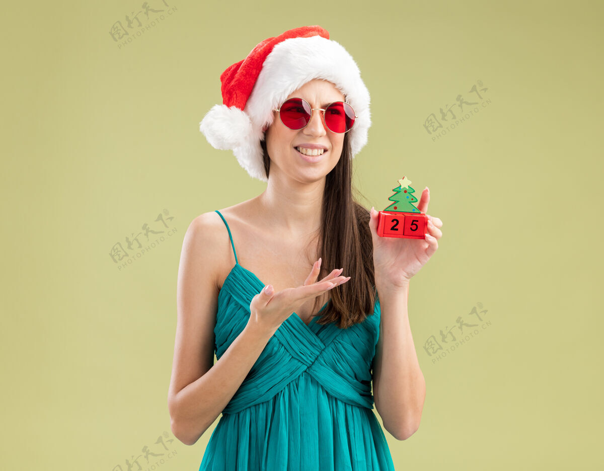 指向戴着太阳眼镜 戴着圣诞帽 手拿圣诞树饰物的白人少女眼镜橄榄手