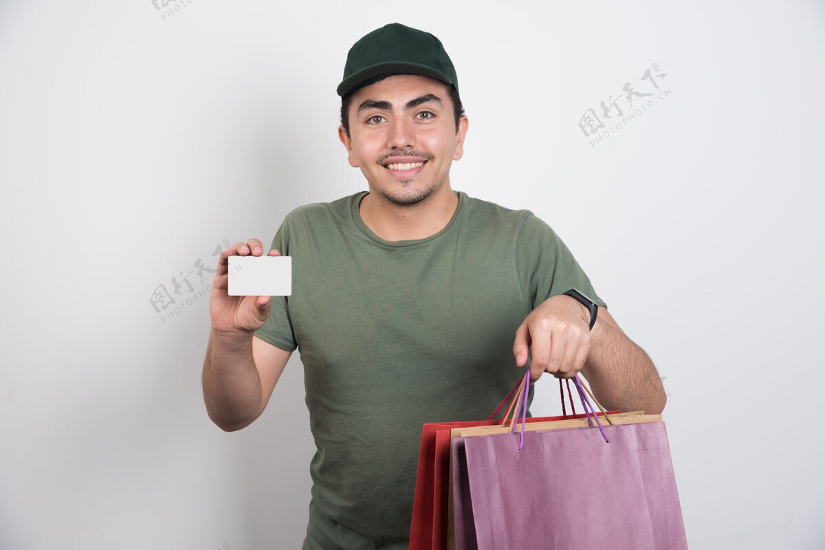 成人一个拿着信用卡和购物袋的年轻人 背景是白色的年轻购物微笑